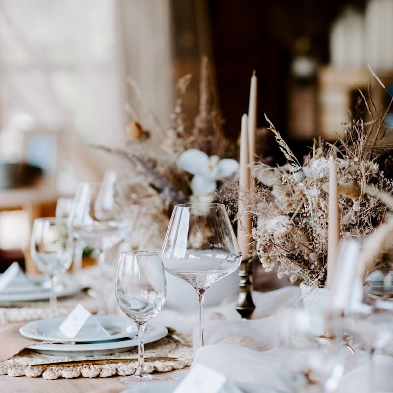 A reception table set with pale linens, glassware and dried florals.